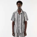 Camisa de manga corta con cuello solapa y cierre frontal de botones, con diseño de rayas verticales en tonos negro y blanco.