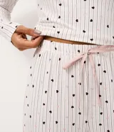 Pantalón de pijama tipo jogger con estampa de corazones pequeños sobre fondo claro, confeccionado en tejido suave al tacto. Presenta cintura elástica con cordón ajustable y puños en los tobillos.