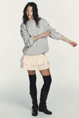 Vestido corto que combina una parte superior tipo sudadera gris de manga larga con puños, y una falda corta de volantes color crema. La parte superior es de tejido de punto jaspeado y la falda tiene dos capas de volantes.