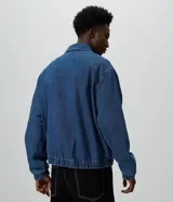 Campera estilo bomber de jean color azul, con cierre frontal, cuello camisero, puños y ruedo con elástico, de corte boxy amplio y estructurado.