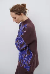 Buzo de tejido de punto con diseño floral en contraste, cuello redondo y mangas largas. Presenta una textura suave y un corte holgado.