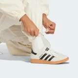 Pantalón deportivo Adidas de corte holgado en color blanco, con cintura elástica y diseño de tres tiras negras verticales en los laterales que incorporan detalles de red y el logo de la marca.