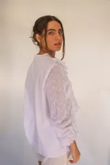 Camisa blanca de algodón estilo romántico con tejido broderie, mangas largas con puños volados y detalles de volados frontales.