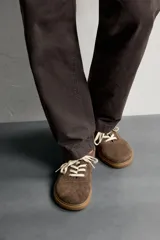 Zapatilla deportiva barefoot fabricada en piel con acabado serraje de color marrón, con cordones en contraste y suela fina de goma.