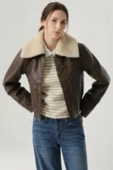 Campera estilo aviador de cuero sintético en color marrón, con cuello de corderito sintético en tono crema, cierre frontal metálico y bolsillos laterales.