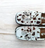 Mocasines de cuero con estampado animal print de vaca, con borlas decorativas y suela plana.