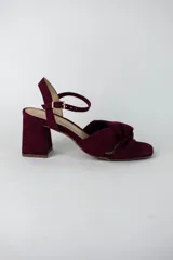 Sandalia de tacón cuadrado medio, confeccionada en material textil tipo gamuza color negro. Presenta un diseño de tiras cruzadas con nudo en la parte delantera y una tira ajustable con hebilla metálica en el tobillo.