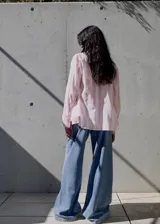 Camisa de corte recto y diseño holgado, con estampado de rayas verticales en tonos blanco y rosado. Presenta cuello camisero clásico, cierre frontal con botones ocultos y mangas largas.