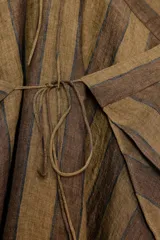 Top de lino 100% con diseño a rayas en tonos marrones. Presenta un cuello halter con tirantes finos que se atan en la espalda y un bajo asimétrico con caída fluida.