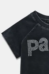Camiseta de algodón con efecto lavado, cuello redondo y manga corta. Presenta un diseño con la palabra 'paris' formada por tachas metálicas.