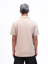Camisa de manga corta color beige, confeccionada en tejido piqué de algodón, con cuello cubano y un bolsillo de parche en el pecho.