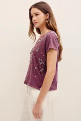 Remera de algodón color morado, con mangas cortas, cuello redondo y bordado de cuentas y pedrería en la parte frontal.