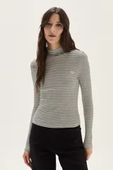 Polera de manga larga con cuello alto, confeccionada en tejido de punto acanalado con diseño de rayas horizontales en color marrón y turquesa. Presenta un bordado pequeño en el pecho y un calce ajustado al cuerpo.