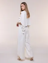 Pantalón palazzo cruzado color blanco con trama en hilo metalizado lurex, cintura elastizada con cordón ajustable con borlas y diseño de piernas anchas con bordes de puntilla y tajo profundo en el frente.