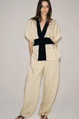 Pantalón de tiro medio Zara Woman Collection, con fajín negro a contraste, pliegues delanteros, pernera ancha, bolsillos laterales ocultos y cierre lateral con cremallera.