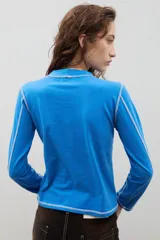 Remera de cuello alto y manga larga en color crudo, con costuras a la vista en contraste de color marrón.