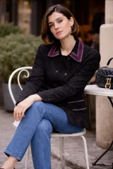Chaqueta de gamuza negra con doble botonadura frontal y detalles de terciopelo en color violeta en el cuello y los bolsillos. Posee mangas largas con botones en los puños.