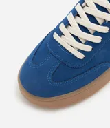 Championes deportivos de mujer modelo chuteira, color azul con aplique lateral en forma de 'V' blanca. Presenta capellada de gamuza sintética, cordones blancos y suela gruesa de goma color caramelo.