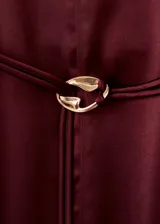 Vestido midi de tejido satinado en color bordó, de corte recto con manga larga, cuello alto y abertura en el bajo delantero. Incluye un cinturón ajustable delgado con detalle metálico dorado.