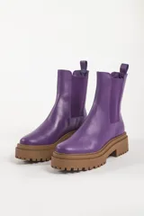 Bota tipo chelsea con suela track de goma en color marrón y capellada de cuero negro. Presenta elásticos laterales y tirador trasero.
