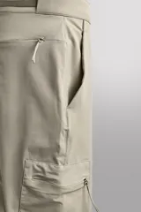 Pantalón de hombre color marrón oscuro, corte regular fit, confeccionado en tejido técnico compacto elástico. Presenta cintura ajustable con cinturón negro a contraste, bolsillos frontales, bolsillo trasero con cierre y bolsillo cargo con cierre en la pernera.