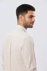 Camisa de lino a rayas finas en tonos beige y blanco, de manga larga con puños vueltos, cuello camisero y cierre frontal de botones. Cuenta con un pequeño logo bordado en el pecho.
