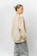 Buzo oversize de algodón frizado color beige, con cuello redondo, puños y cintura tejidos. Presenta un bordado tono sobre tono de Garfield en el frente.