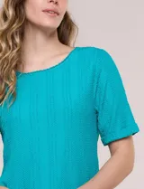 Blusa blanca de tejido de punto liviano con textura labrada en franjas verticales y caladas, de silueta evasé, con escote redondo, manga corta y ruedo asimétrico en picos.