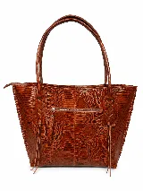 Cartera tipo tote bag de cuero vacuno marrón, con detalles de trenzado artesanal en los laterales y flecos colgantes decorativos. Cuenta con doble asa de hombro y cierre superior.