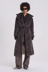 Tapado largo de piel sintética color gris topo, con cuello solapa, lazo de cuero sintético negro en la cintura y forro de tafeta con logo de la marca.