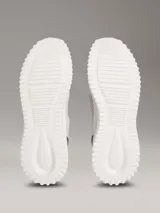 Zapatillas tipo runner Calvin Klein, de color gris con detalles en negro y coral. Presentan un diseño de malla perforada en la parte superior, cordones negros, suela chunky de EVA blanca y el logo de la marca en la lengüeta y el lateral.