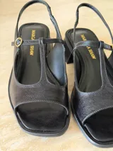 Sandalia de gamuza color marrón, con diseño tipo T-strap, taco cuadrado bajo y tira ajustable al talón con hebilla metálica dorada.