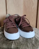 Zapatillas plateadas de cuero con cordones grises y suela blanca.