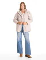 Campera 3 en 1 de color beige, con sistema de capas desmontables. La capa exterior es de tejido técnico resistente al viento y lluvia ligera, con capucha fija, cierre frontal con solapa, bolsillos de parche y ajuste elástico interno en la cintura. Incluye una campera interior capitoneada ultraliviana que puede usarse de forma independiente.