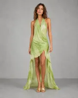 Vestido largo asimétrico de estilo etéreo, con escote halter cruzado y espalda descubierta. Presenta un diseño corto en la parte frontal y una cola larga en la parte posterior, confeccionado en una tela ligera con estampado abstracto en tonos verdes.
