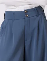 Pantalón de corte palazzo en color verde militar, con tiro alto, doble abotonadura frontal y pinzas. Presenta una silueta de pierna ancha, bolsillos laterales funcionales y cintura elástica en la parte posterior.