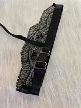 Accesorio tipo collarín de encaje negro con diseño floral, cuenta con una banda ajustable para el cuello y una tira que desciende hacia el pecho.