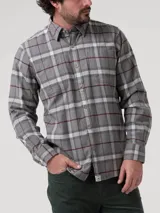 Camisa de manga larga confeccionada en franela de algodón orgánico cepillado, con diseño de cuadros en tonos grises, blancos y líneas finas en color bordó. Presenta cuello clásico, cierre frontal con botones de madera y dos bolsillos frontales en el pecho.