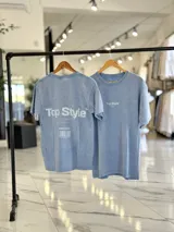 Remera oversize de efecto gastado color celeste, con cuello redondo y mangas cortas. Estampado frontal pequeño con el texto "Top Style" y gran estampado en la espalda con el mismo texto, la frase "Dream big. Work hard. Make it real.", el año "SINCE 2021" y un código de barras.