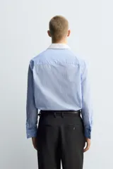 Camisa de corte regular fit confeccionada en algodón, con estampado de rayas verticales en tonos azul y blanco. Presenta cuello italiano en color blanco a contraste, cierre frontal de botones y mangas largas con puños dobles.