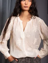 Blusa de tela liviana color crudo, con bordados florales tono sobre tono, escote en V con detalle de puntilla central, mangas largas con volumen y puños camiseros.
