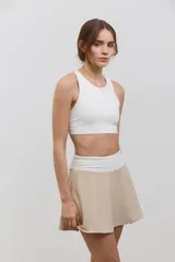 Pollera deportiva de corte acampanado color beige, con calza corta integrada de color blanco. Presenta cintura ancha de tiro alto y bolsillo invertido en la calza para guardar pelotas.