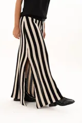 Pollera larga de tejido de punto con diseño de rayas verticales en color negro y crudo. Presenta una pretina elástica con cordón de ajuste y tajos laterales profundos que aportan movimiento.