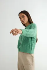 Cardigan de punto gris con diseño de ochos y trenzas, cuello redondo y cierre frontal con botones dorados grandes. Posee mangas largas con puños acanalados.