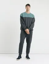 Sweater de tejido circular con diseño color block, combinando una franja superior en color verde y el resto de la prenda en gris oscuro. Presenta cuello redondo y puños en tejido canalé.