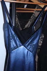 Vestido largo de satén y encaje color azul, con corte bajo el busto, escote en V con detalles de encaje transparente, tirantes finos cruzados y corte en la cadera.