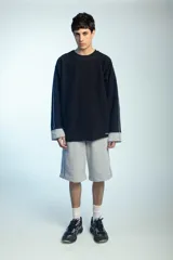 Buzo de felpa negro de corte oversize, con cuello redondo y mangas largas con puños grises doblados hacia afuera. Presenta costuras externas decorativas en tono gris claro a lo largo de las mangas y los hombros.