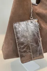 Bolso tipo tote de gamuza en color verde oliva, con diseño minimalista y asa integrada. Presenta una placa metálica con el logo de la marca en la parte inferior central y detalles de textura en el asa.