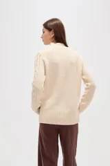 Polera de tejido de punto color crema, con cuello alto y diseño de trenzas verticales. Presenta mangas largas con puños acanalados y un corte holgado.