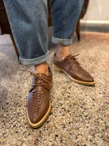 Zapato acordonado color marrón, con suela plana y cordones finos.